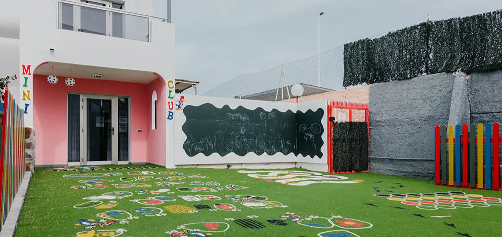 &Aacute;rea de juegos infantil con c&eacute;sped artificial y una pizarra al aire libre.