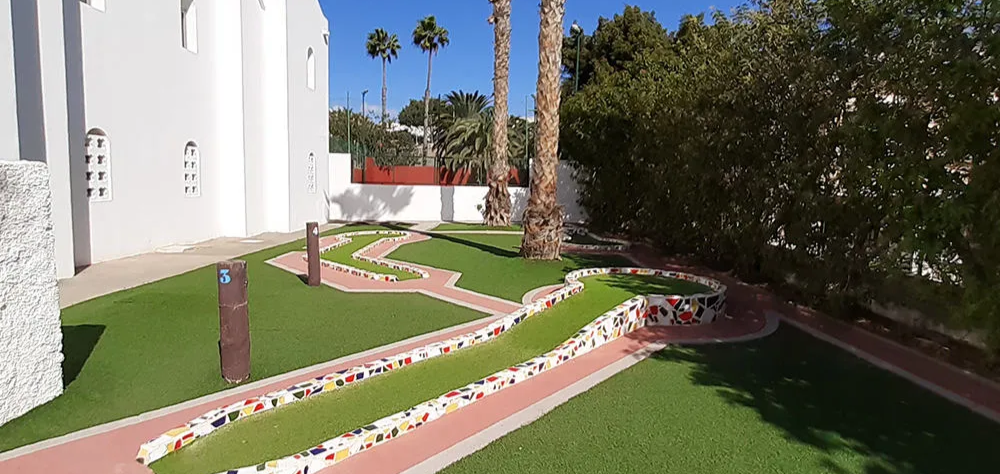 Campo de minigolf al aire libre con caminos y palmeras alrededor.