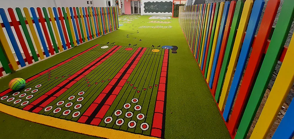 Patio de juegos con c&eacute;sped artificial y valla de colores.