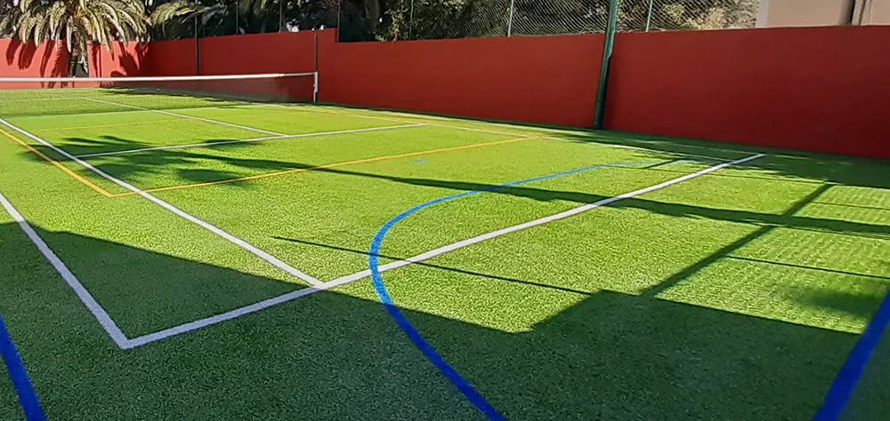 Cancha de c&eacute;sped sint&eacute;tico con l&iacute;neas de juego y paredes rojas alrededor.