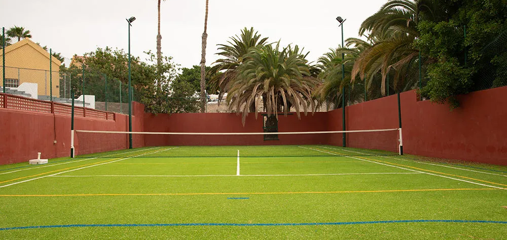 Cancha de tenis rodeada de palmeras y muros rojos.