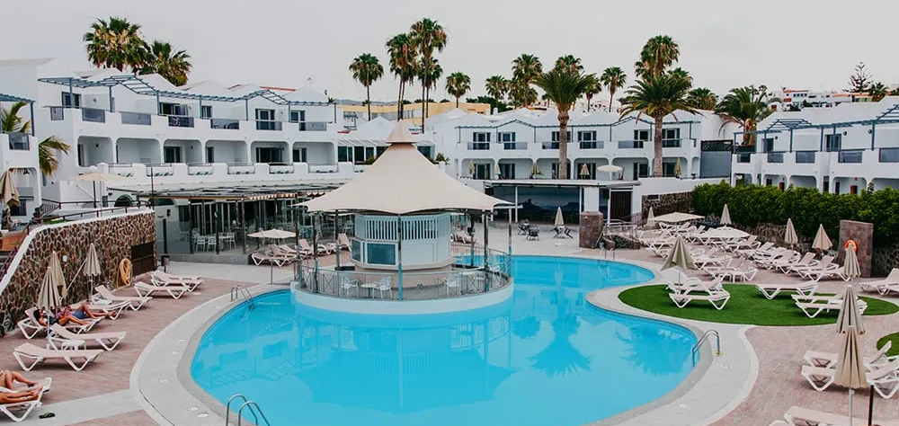 Piscina en hotel con tumbonas blancas y palmeras alrededor.