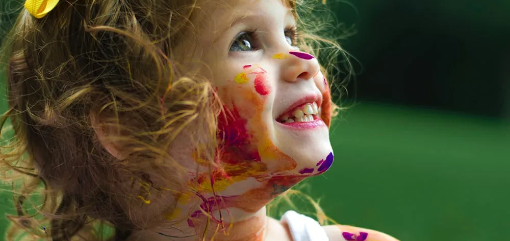 Ni&ntilde;a sonriente con pintura de colores en el rostro sobre fondo verde.