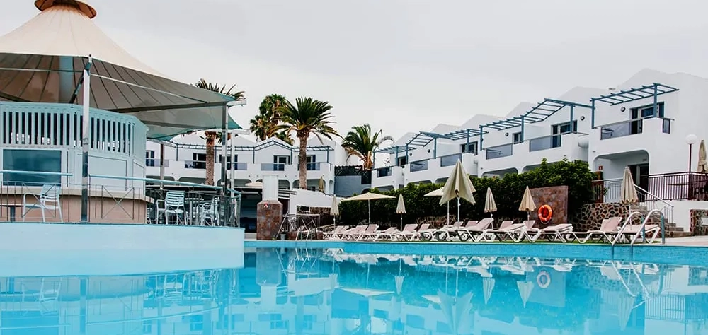 Piscina frente a hotel moderno con sombrillas y tumbonas.