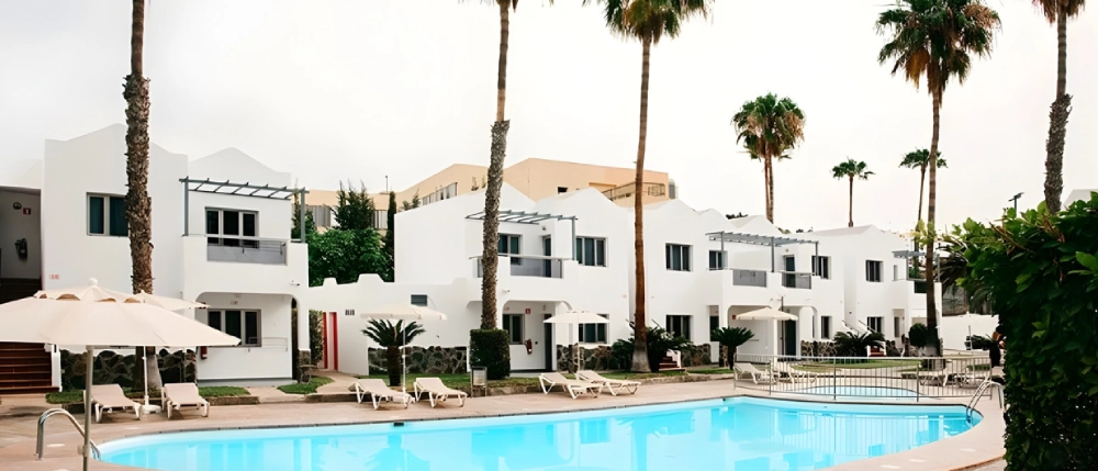 Conjunto de casas blancas con piscina y palmeras alrededor.
