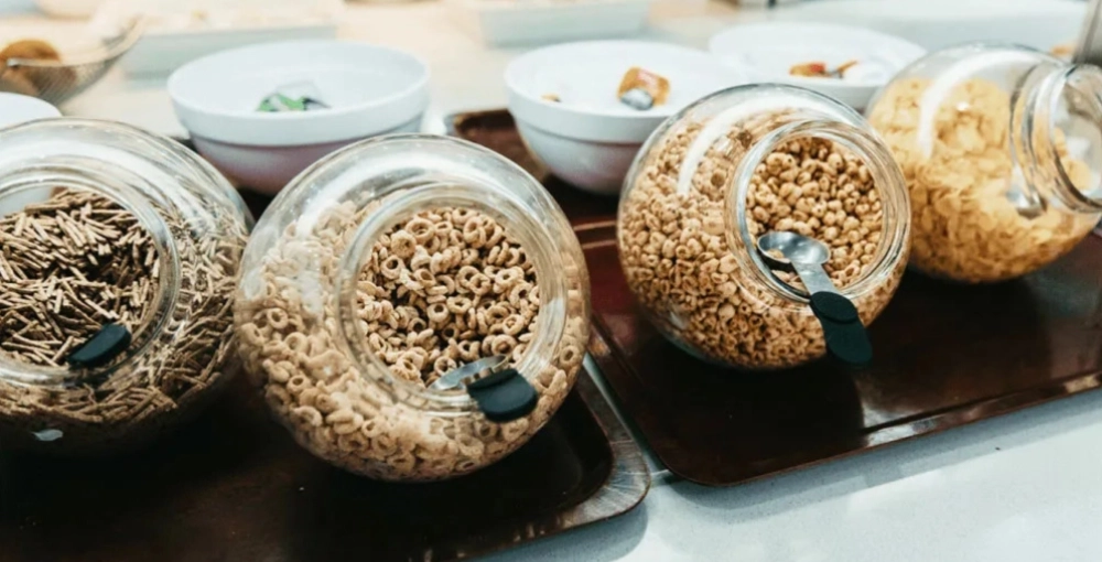 Frascos de vidrio con cereales diversos y cucharas en una mesa.