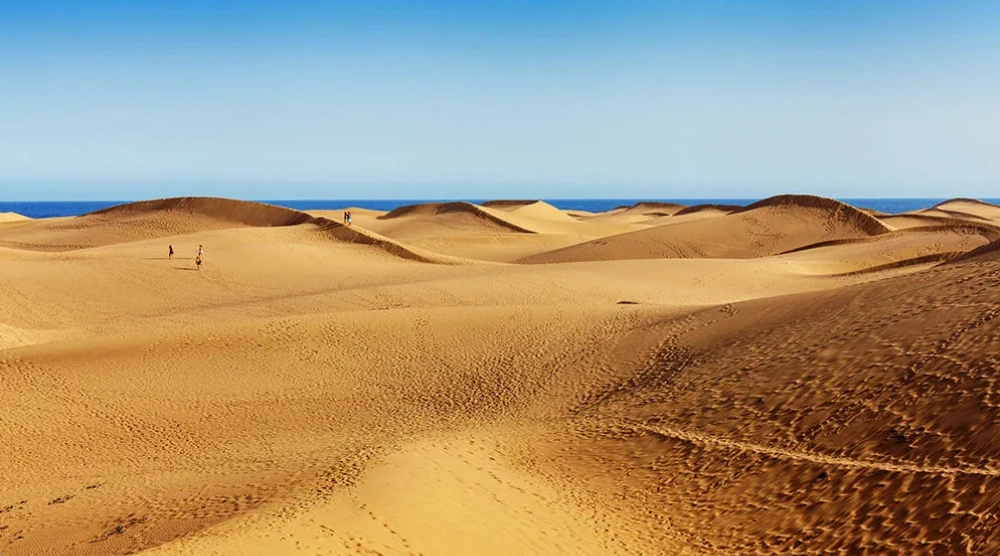 Dunas doradas con el oc&eacute;ano al fondo y un cielo despejado.