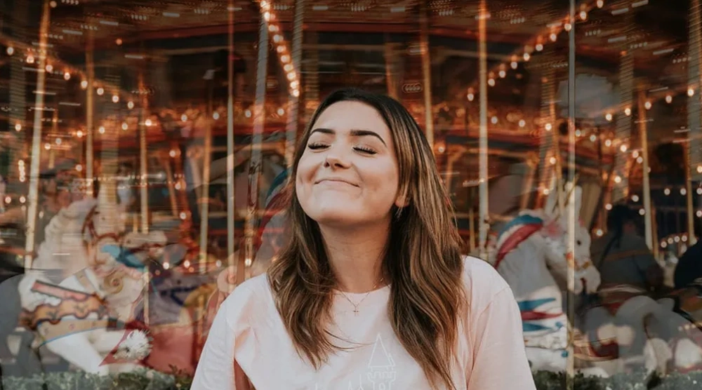 Mujer sonriendo frente a un carrusel iluminado.