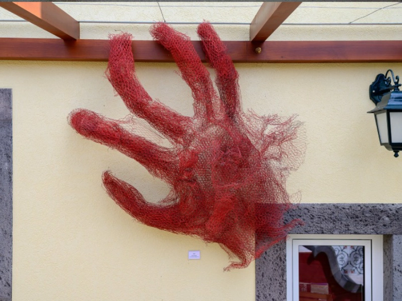Red wire hand sculpture on a beige wall above a doorway.
