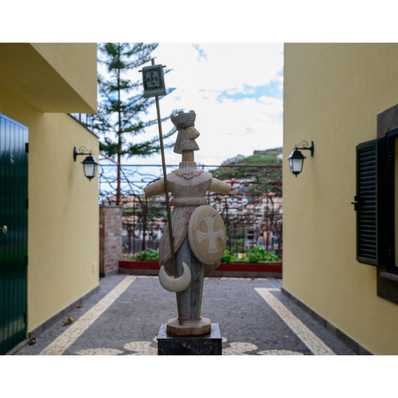Stone knight statue in an alley with yellow walls and a tree in the background.