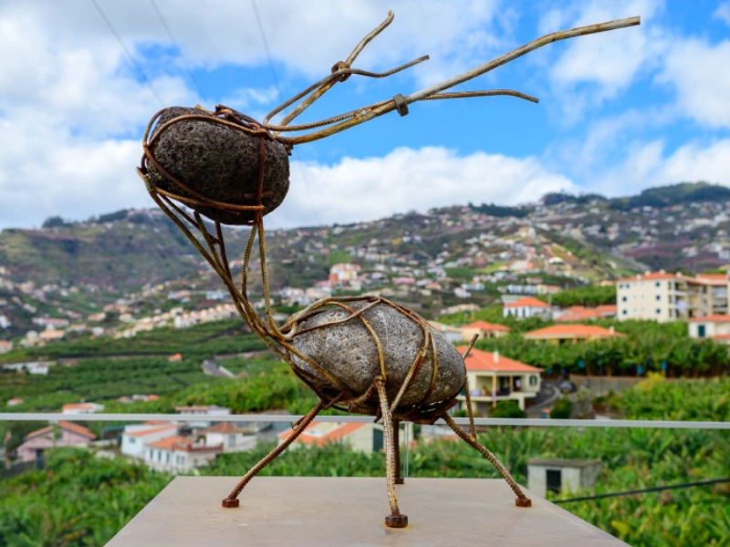 Stone and metal sculpture resembling an animal on a scenic hillside background.