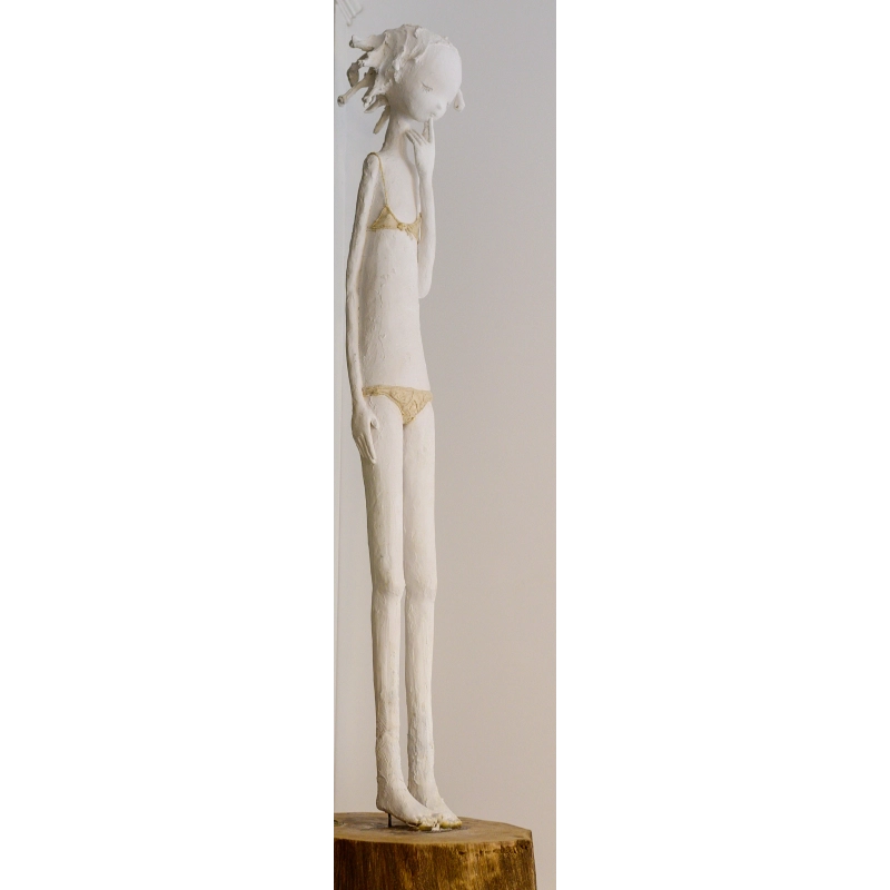 White sculpture of a thoughtful figure wearing a bikini, standing on wooden base.