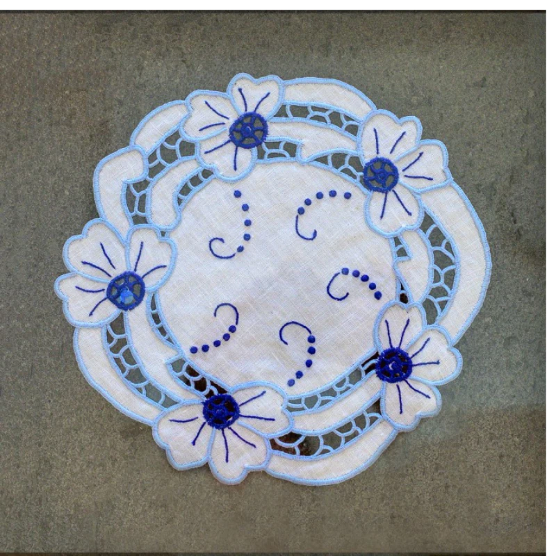 White doily with blue embroidered flowers and curves.