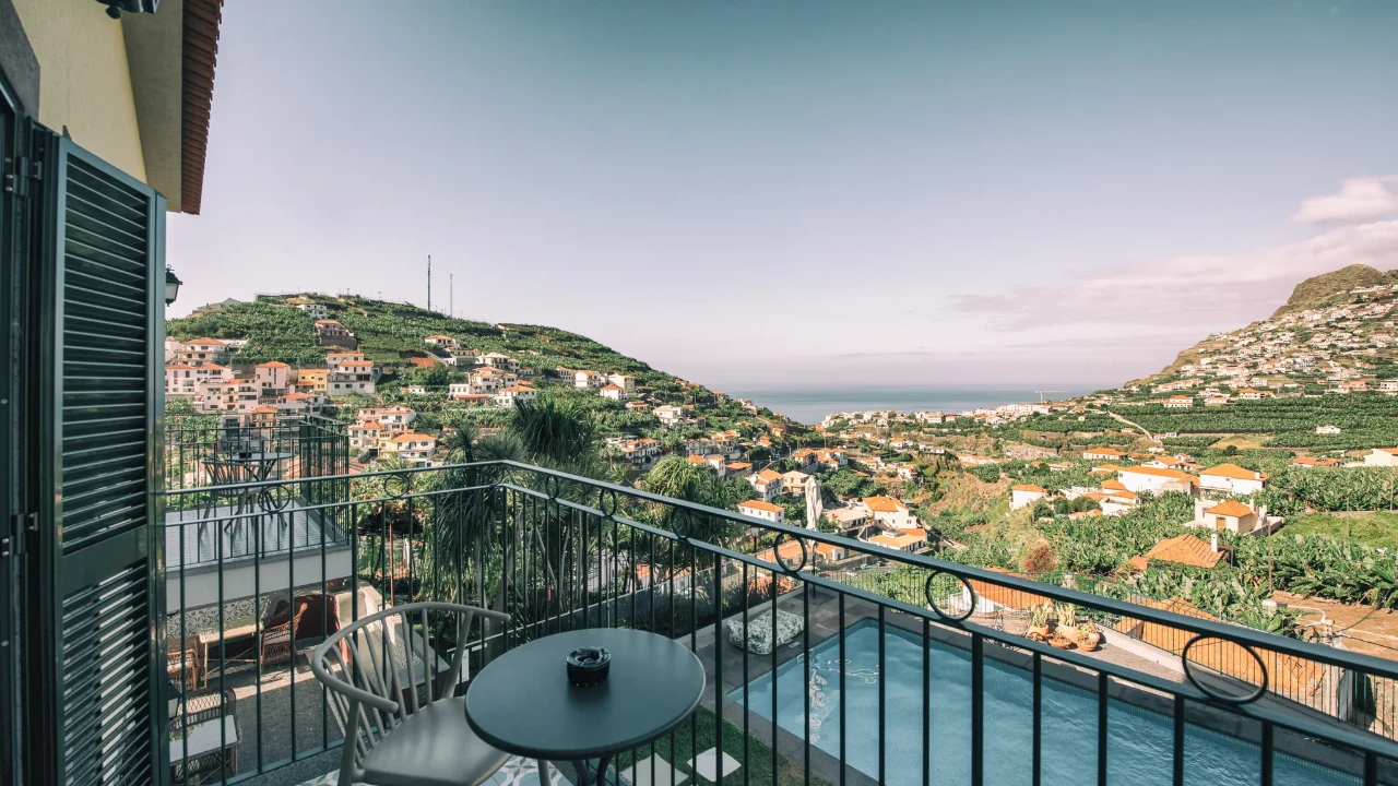 Balcony overlooking hills, houses, a pool, and the ocean under a clear sky.