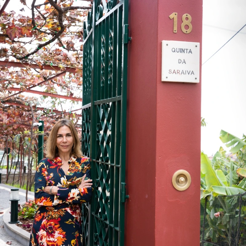 Woman in floral dress stands by a gate labeled "Quinta da Saraiva" number 18.