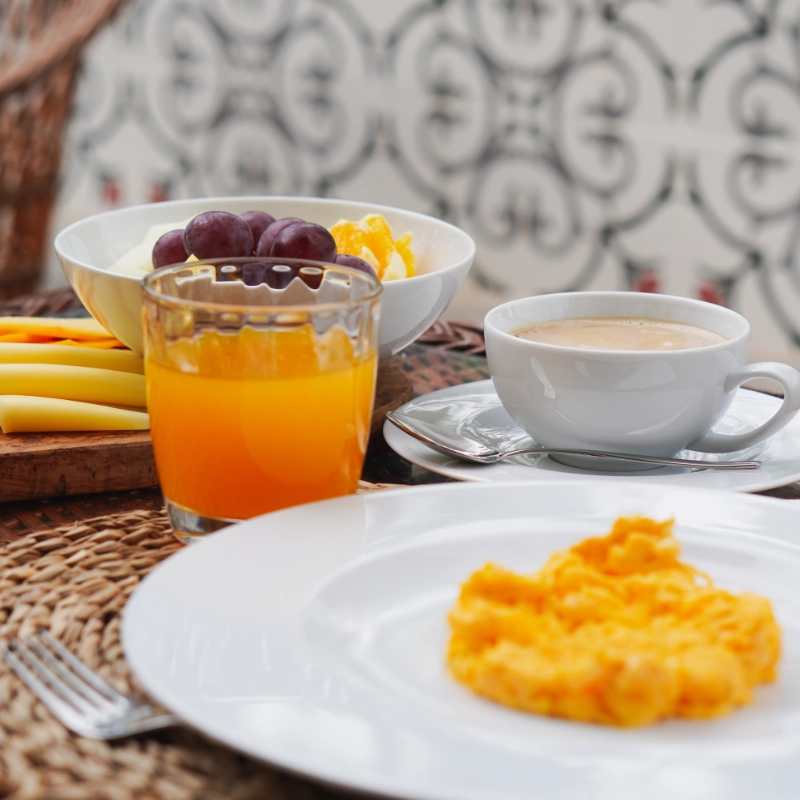 A breakfast with scrambled eggs, orange juice, fruit, and coffee on a table.
