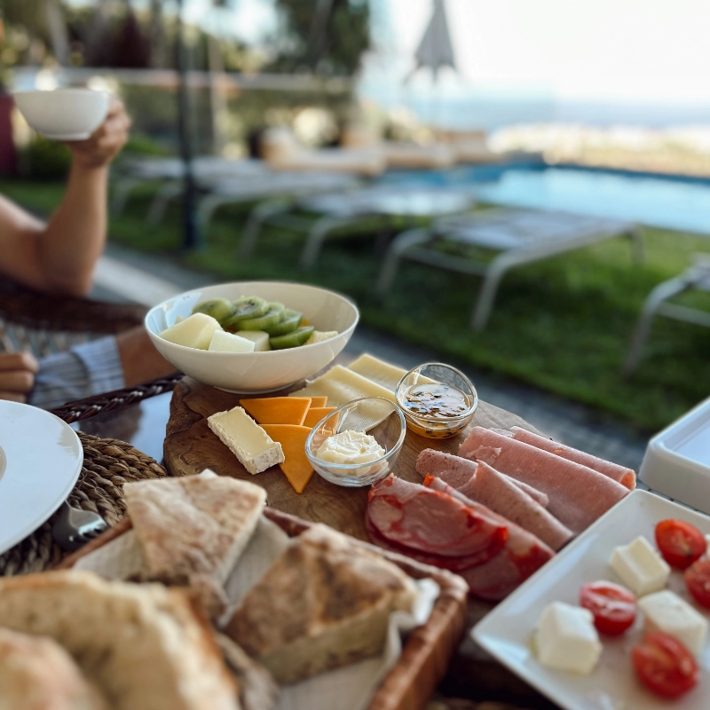 A breakfast spread with meats, cheeses, fruits, and bread by a poolside.