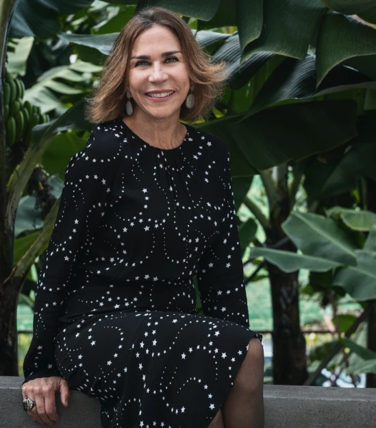 Smiling woman in a starry dress sits by lush green banana leaves.