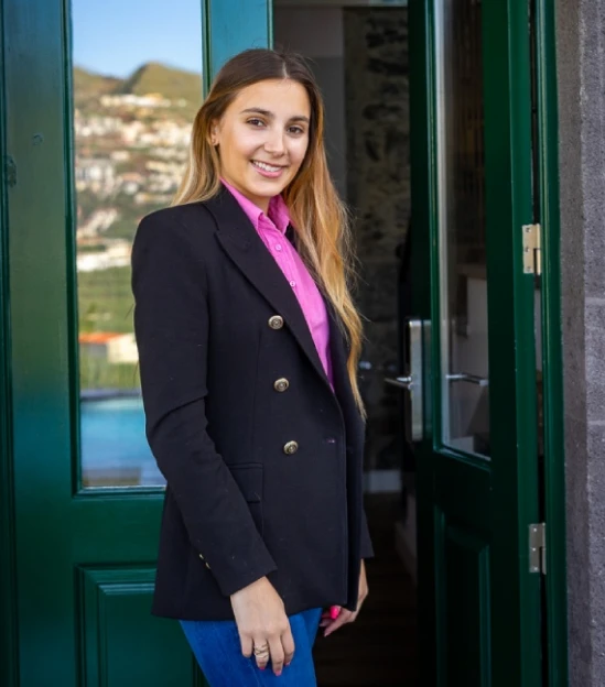 Smiling person in a blazer standing by an open door.