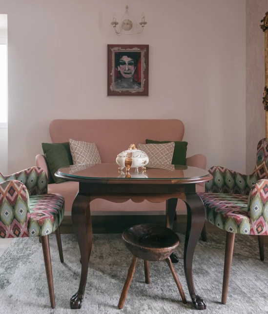 Vintage living room with pink sofa, patterned chairs, and round table.