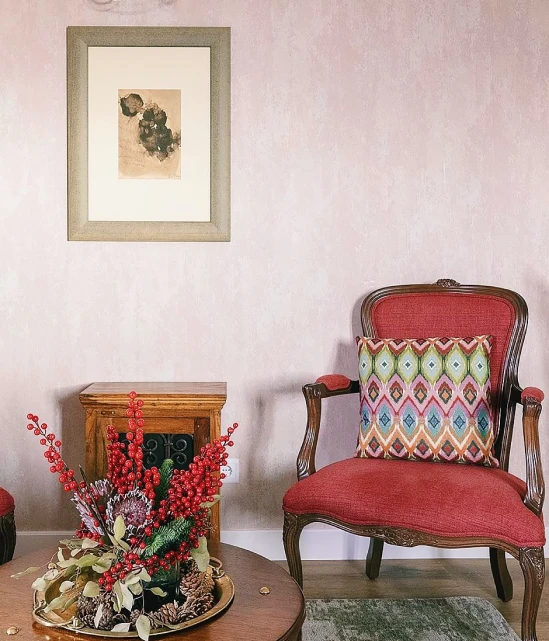 Red chair with patterned pillow, artwork on wall, table with floral arrangement.