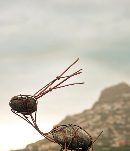 Stone and wire sculpture resembling a bird against a cloudy sky.