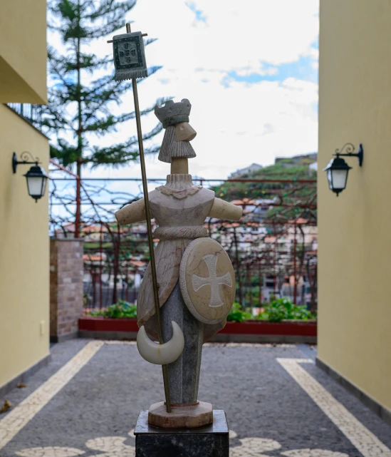 Stone statue with shield and spear in courtyard walkway.