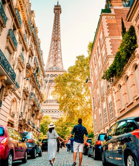 Un couple marche vers la Tour Eiffel dans une rue bord&eacute;e de voitures.