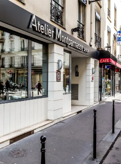 Fa&ccedil;ade de l'H&ocirc;tel Atelier Montparnasse et caf&eacute; voisin sur rue parisienne.