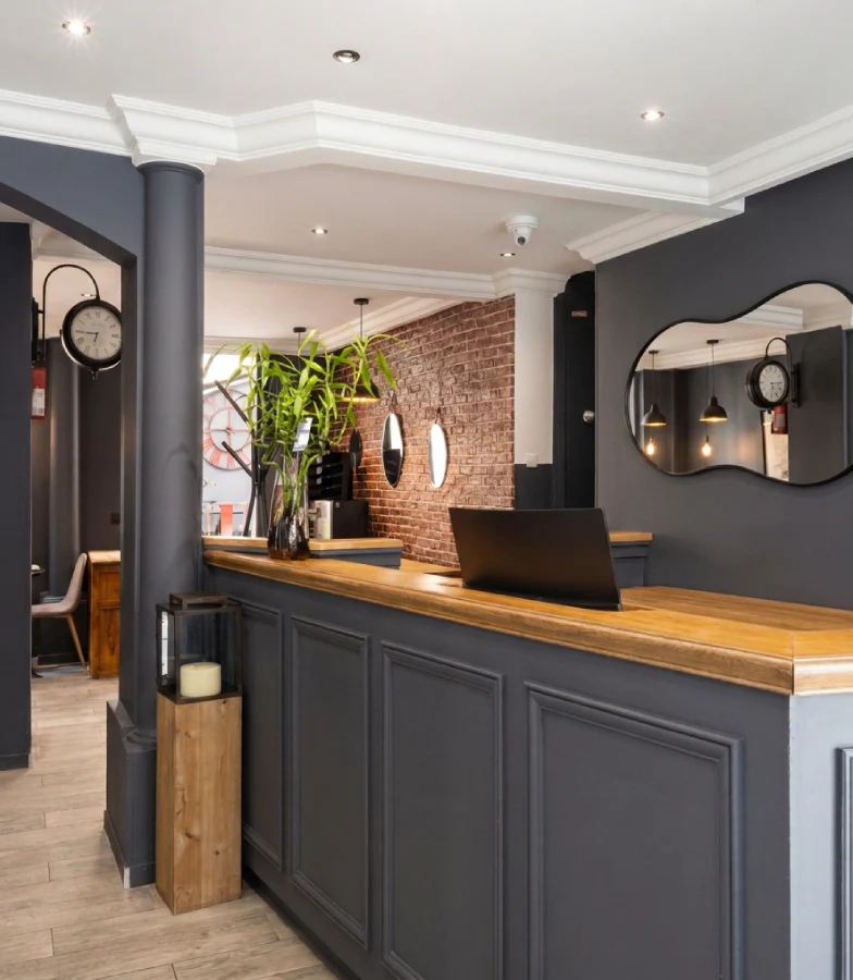 R&eacute;ception d&rsquo;h&ocirc;tel moderne avec comptoir gris, miroir et plantes en int&eacute;rieur.