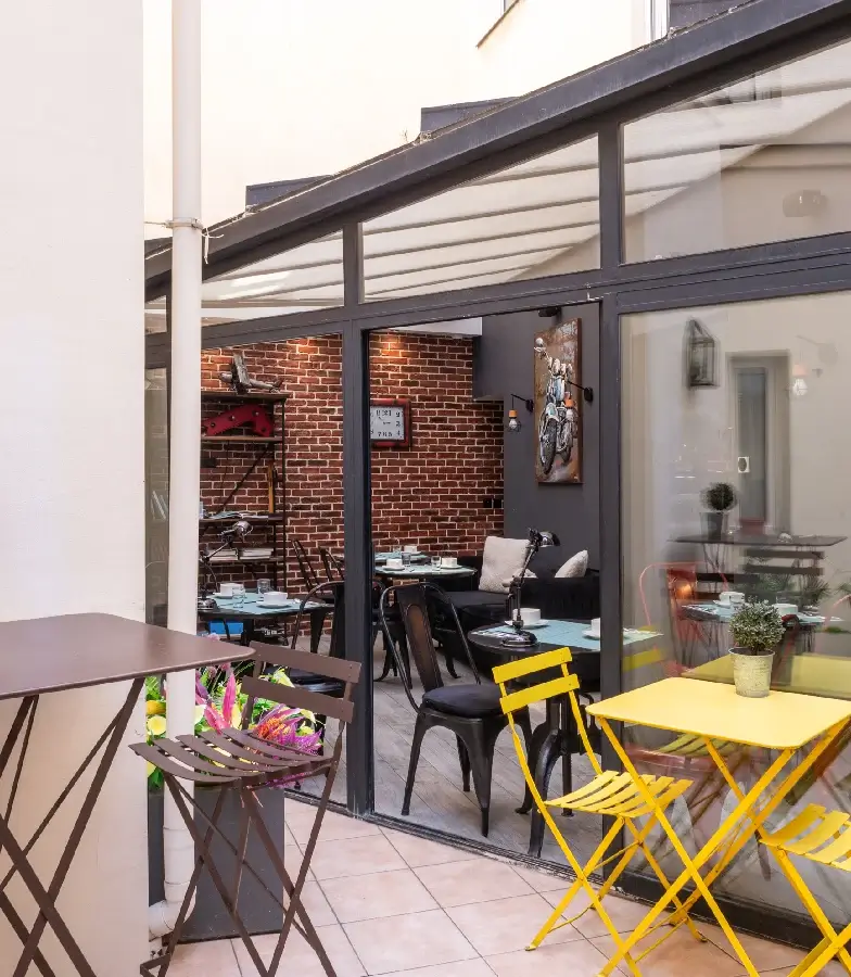 Terrasse urbaine avec tables, chaises jaunes et briques rouges derri&egrave;re une baie vitr&eacute;e