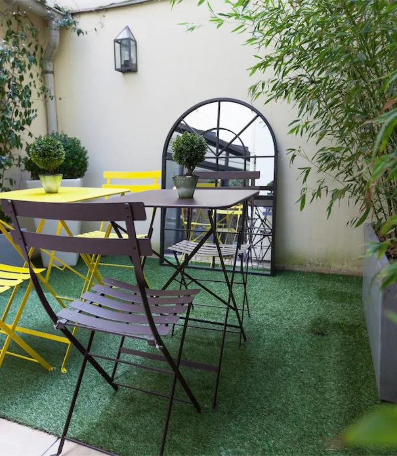 Petit jardin avec table, chaises color&eacute;es et miroir en ext&eacute;rieur.