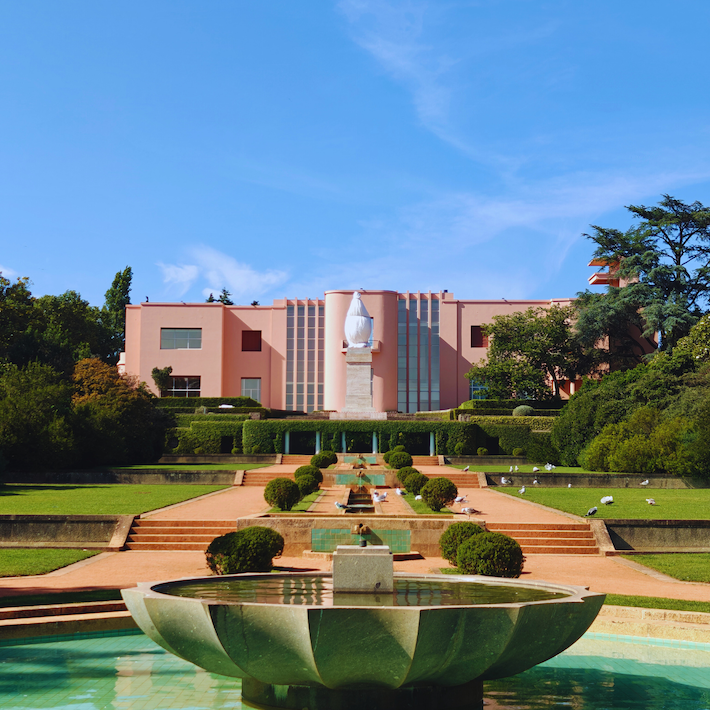 A pink building with gardens and a fountain under a blue sky.