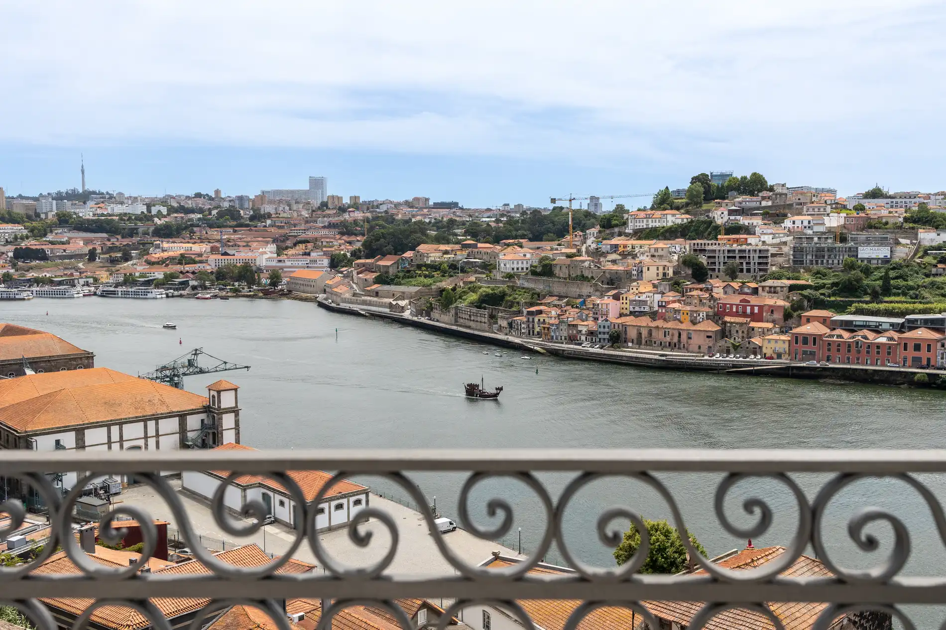 Balcony view of a riverside cityscape with a boat on the water.