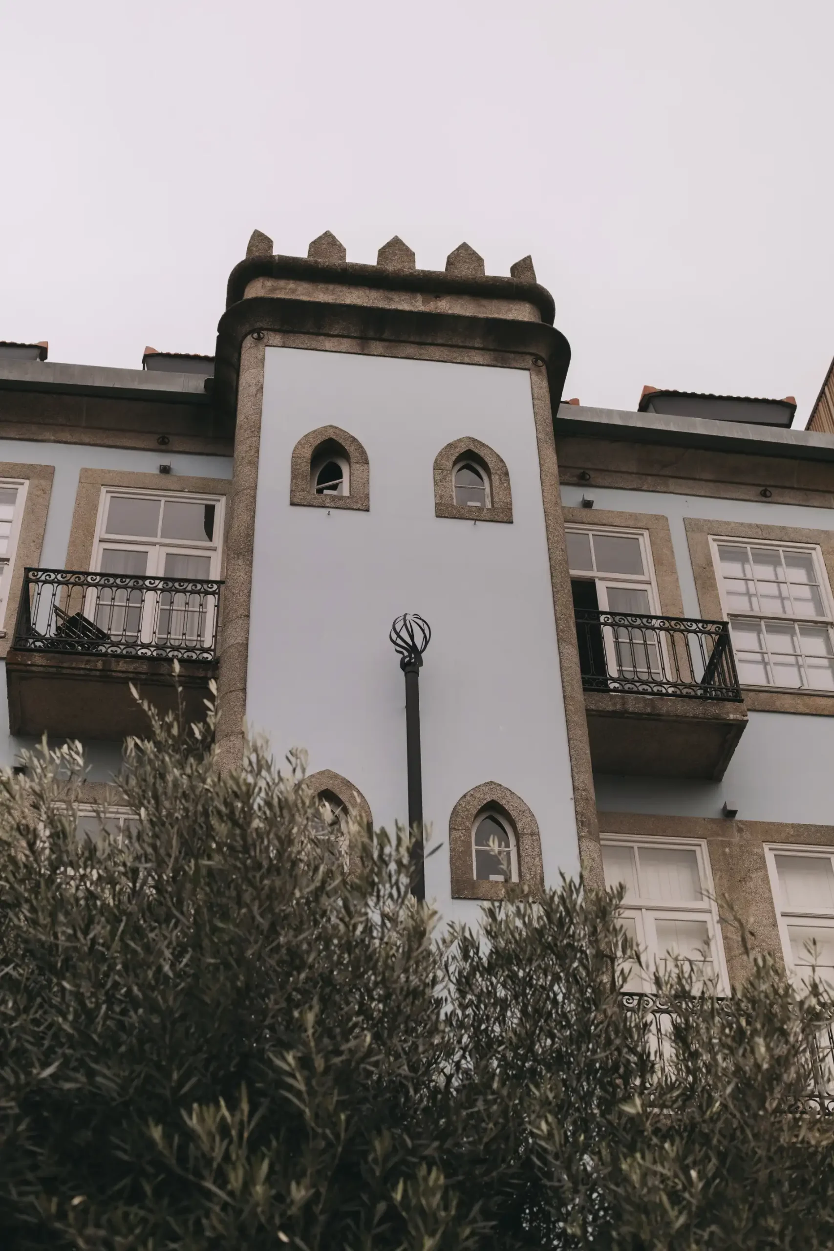 Tall building with arched windows and greenery in foreground.