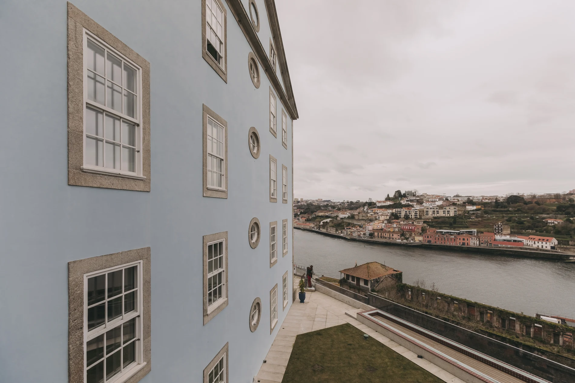 Blue building with windows beside a river, overlooking a townscape.