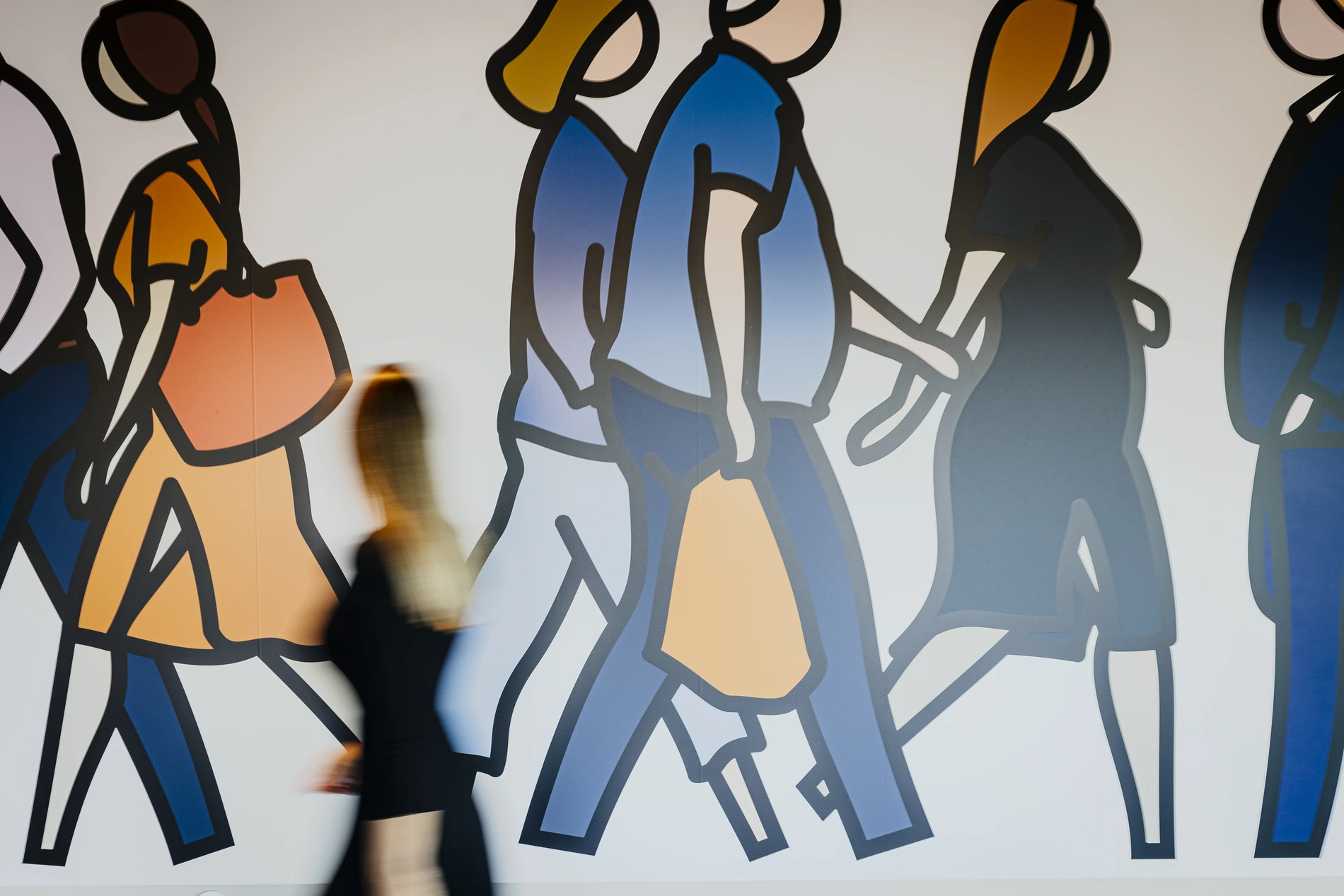 Blurred person walking past colorful wall mural of people.