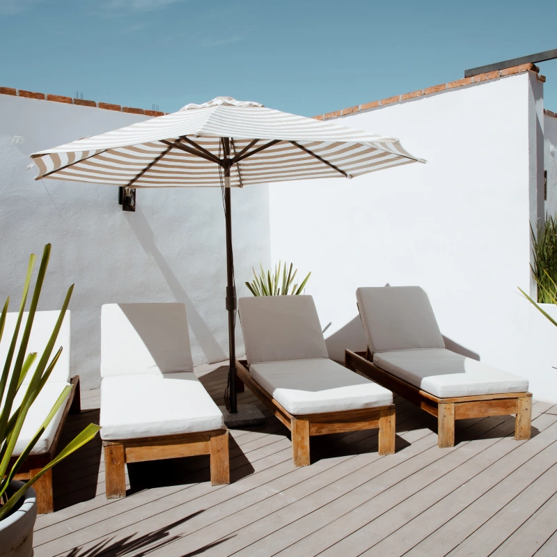 Terraza con tumbonas blancas y sombrilla a rayas bajo un cielo azul.