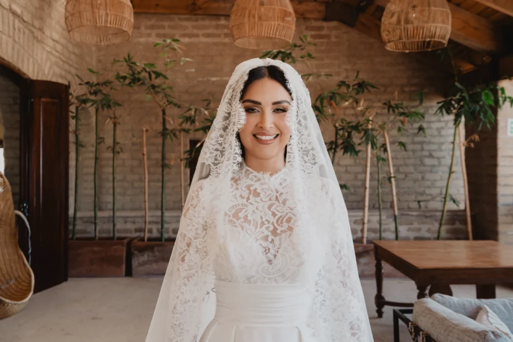 Novia sonr&iacute;e con vestido de encaje y velo en ambiente r&uacute;stico.