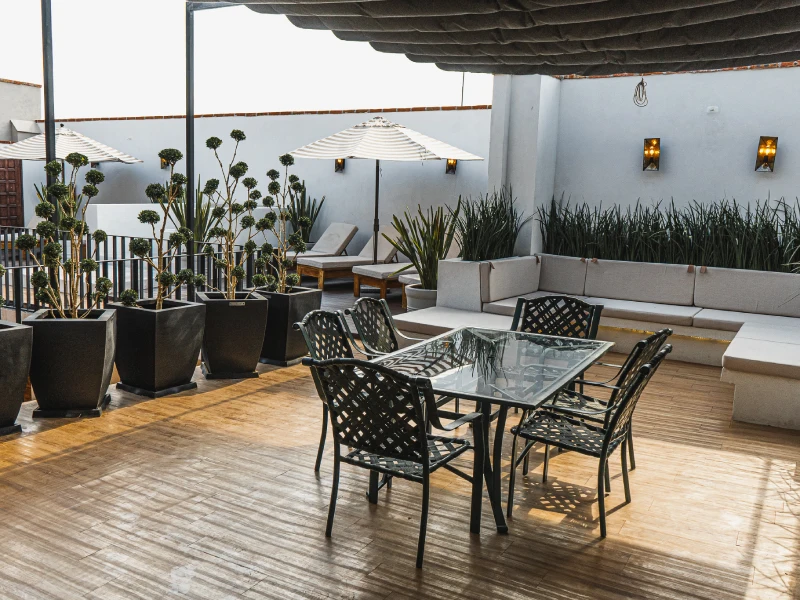 Terraza acogedora con mesa, sillas, plantas y sof&aacute;s bajo sombrillas blancas.
