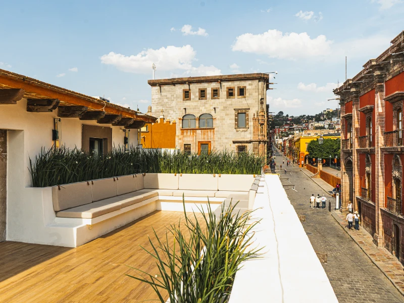 Terraza con plantas, edificios coloniales y calle empedrada bajo un cielo azul.