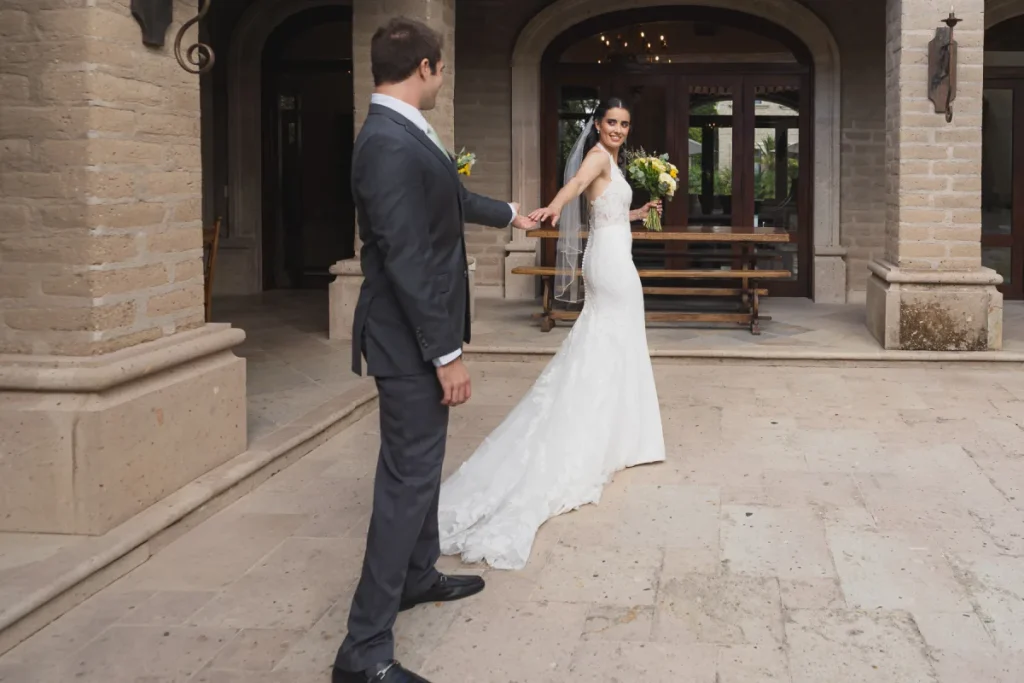 Pareja de novios sonr&iacute;e en un patio mientras se toman de la mano.