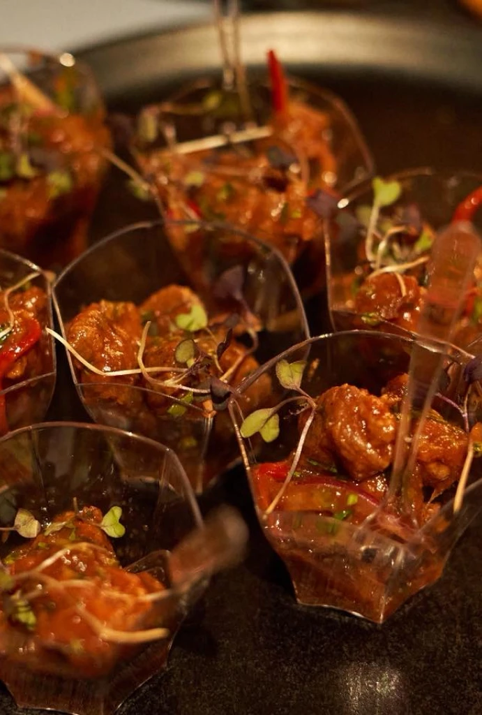 Mini porciones de carne en salsa con brotes en peque&ntilde;os recipientes transparentes.