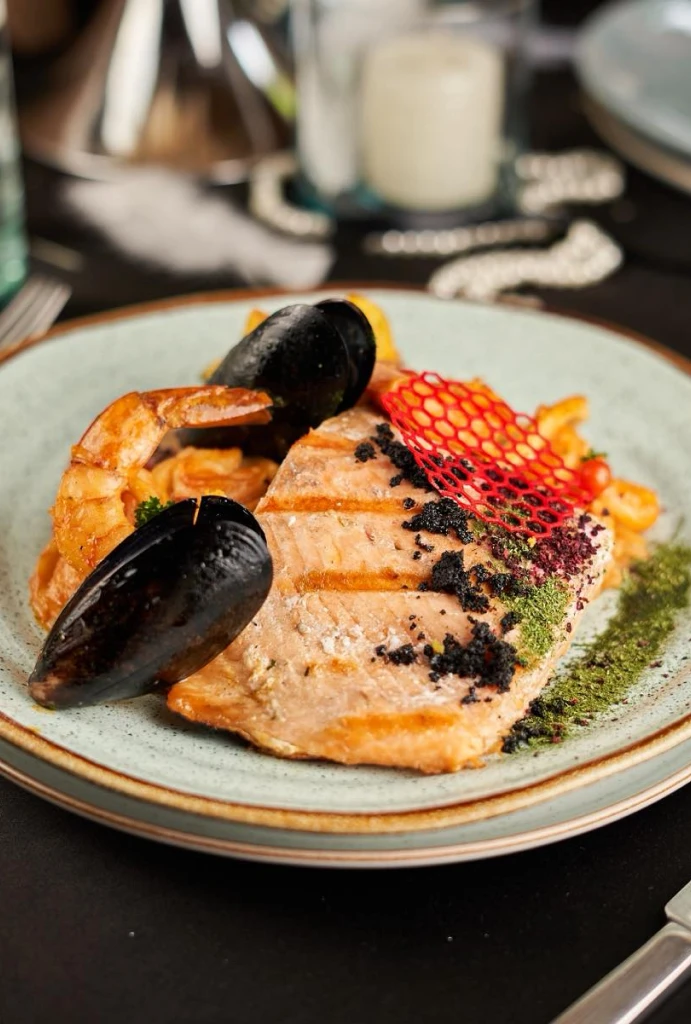 Plato gourmet de salm&oacute;n con mariscos y decoraci&oacute;n art&iacute;stica.