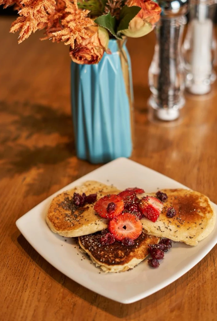 Plato de panqueques con fresas y vaso azul con flores.