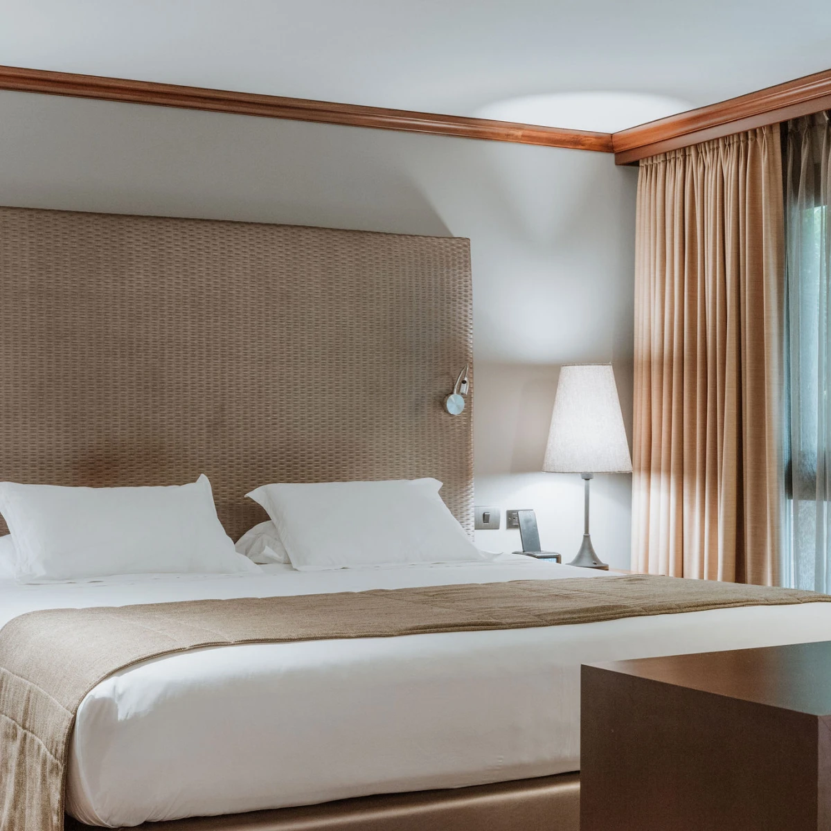 Cama doble con l&aacute;mpara y cortinas en habitaci&oacute;n moderna y acogedora.