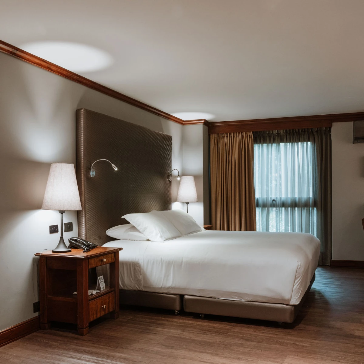 Habitaci&oacute;n de hotel elegante con cama, l&aacute;mparas y ventana con cortinas.