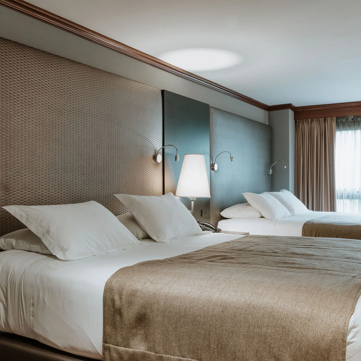 Dos camas de hotel con ropa de cama blanca y l&aacute;mparas de lectura.