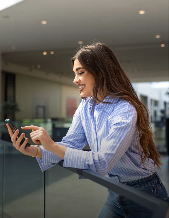Mujer sonriendo mientras utiliza su tel&eacute;fono m&oacute;vil en un espacio interior.
