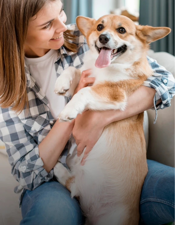 Mujer sonriente abrazando a un perro Corgi que saca la lengua.
